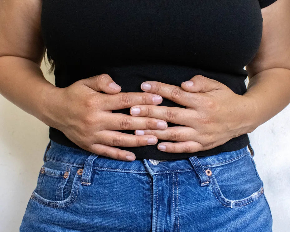 A woman in a black T-shirt and blue jeans rests both hands over her stomach.