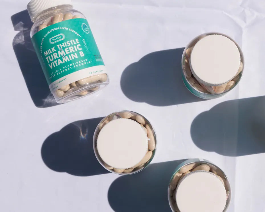 A bottle of The Plug Pills lies on a white surface beside three open capsule lids casting long shadows.