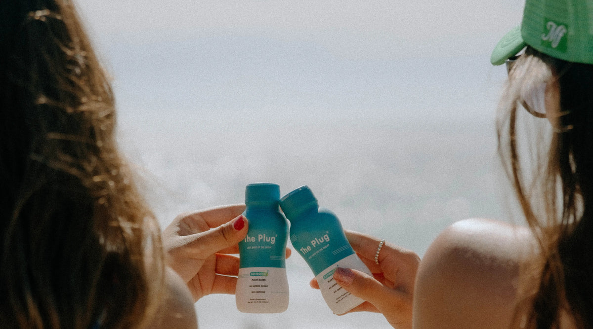 Two friends touching bottles of The Plug Drink together against the sky