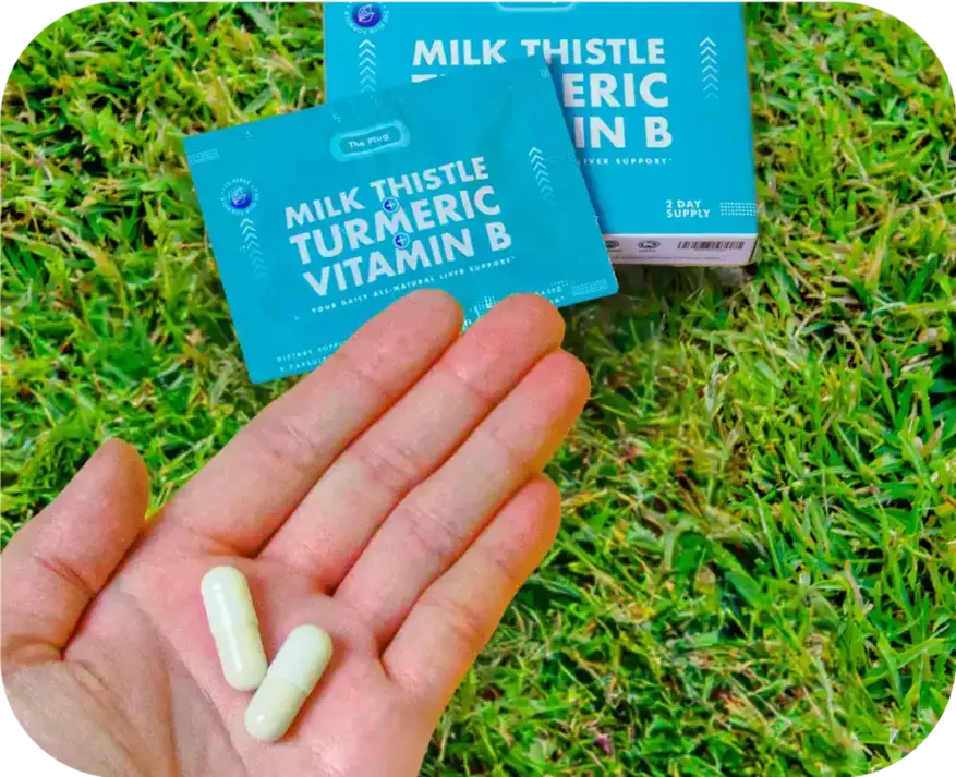 Hand holding two Milk Thistle Turmeric Vitamin B liver support capsules outdoors on grass