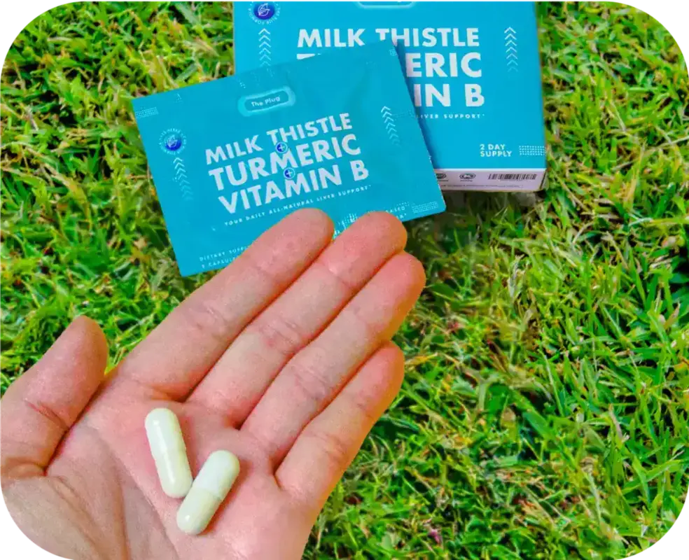 Hand holding two Milk Thistle Turmeric Vitamin B liver support capsules outdoors on grass