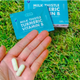 Hand holding two Milk Thistle Turmeric Vitamin B liver support capsules outdoors on grass