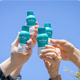 Friends toasting with bottles of The Plug hangover drink against a blue sky