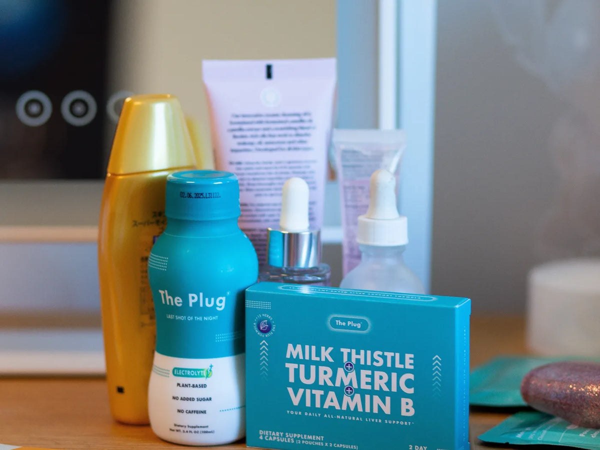 A bottle of The Plug Drink and a box of The Plug Pills stand on a vanity shelf among Korean skincare bottles, a dropper and a tube.