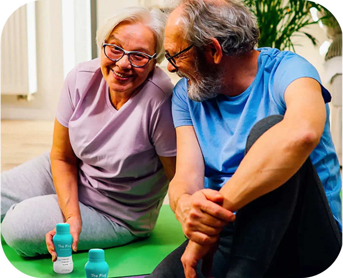 Older couple smiling together on a yoga mat with The Plug liver support drink bottles beside them