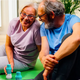 Older couple stretching on a yoga mat with two bottles of The Plug liver support drink