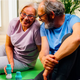 Older couple stretching on a yoga mat with two bottles of The Plug liver support drink