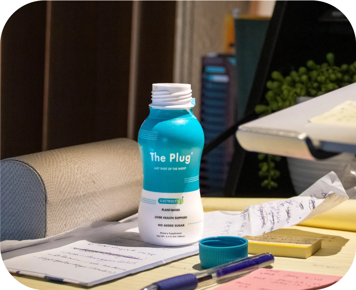 Open bottle of The Plug liver health drink on a desk with notes and a pen