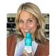 Smiling woman holding The Plug liver support drink bottle in her kitchen