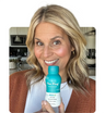 Smiling woman holding The Plug liver support drink bottle in her kitchen