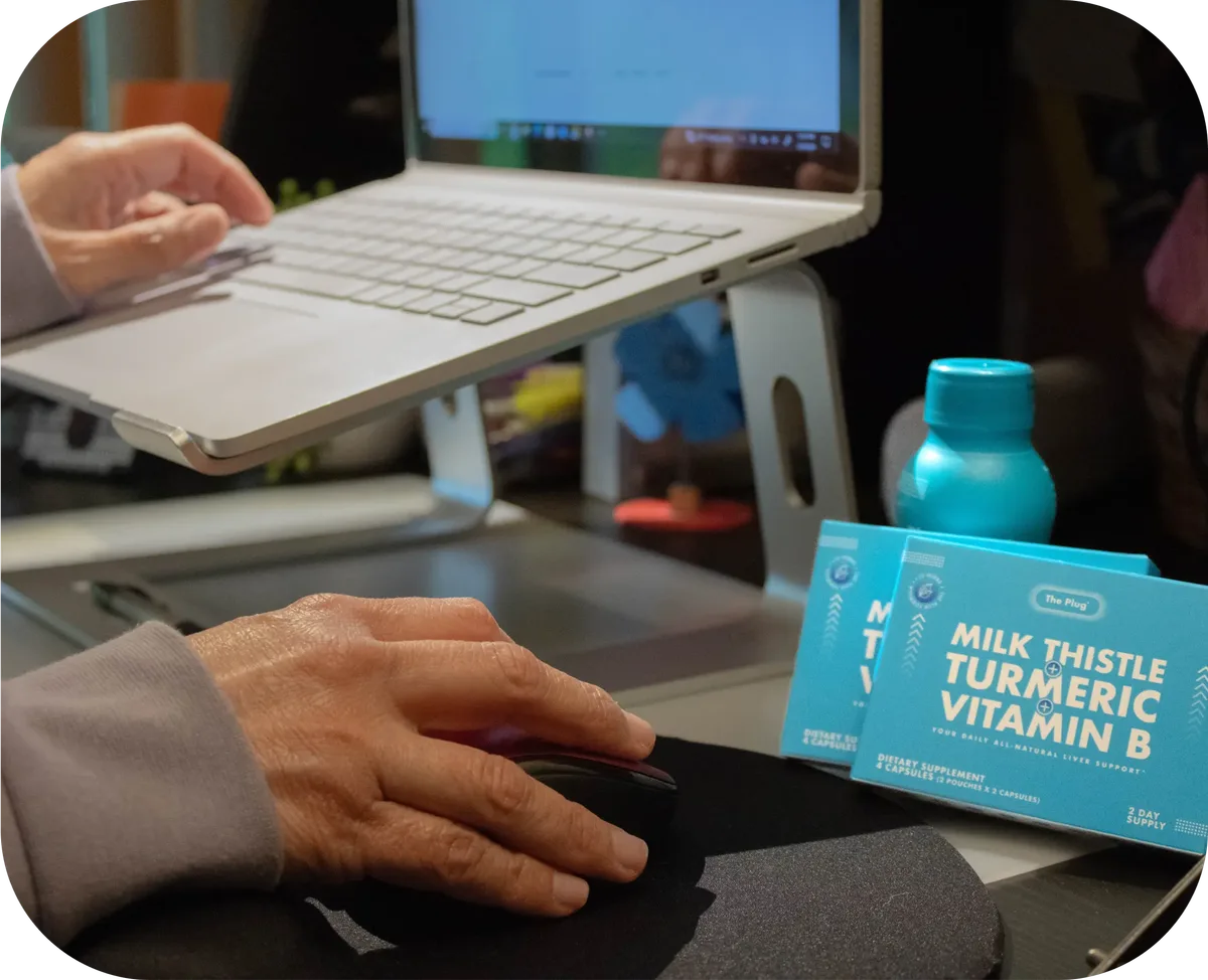The Plug liver support drink bottle and Milk Thistle Turmeric Vitamin B pill boxes on a desk next to a laptop