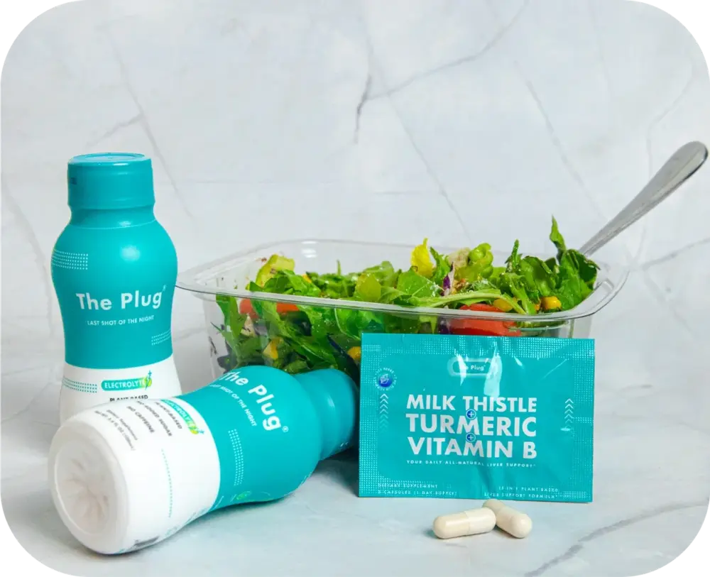 Two bottles of The Plug liver drink next to a fresh salad and milk thistle turmeric vitamin B supplement pack