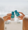 Two hands clinking bottles of The Plug liver support drink on the beach