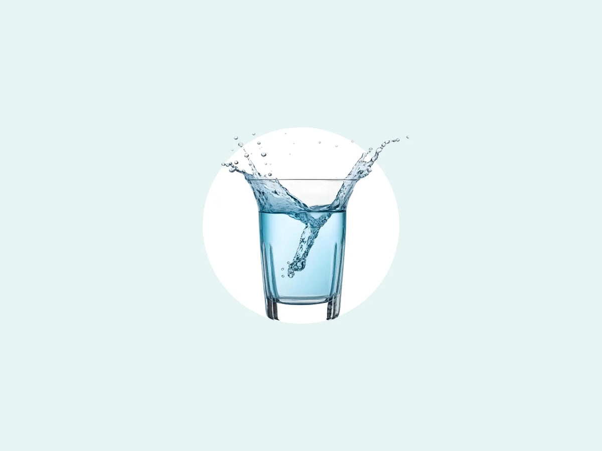 Water splashes into a clear glass against a pale teal background.