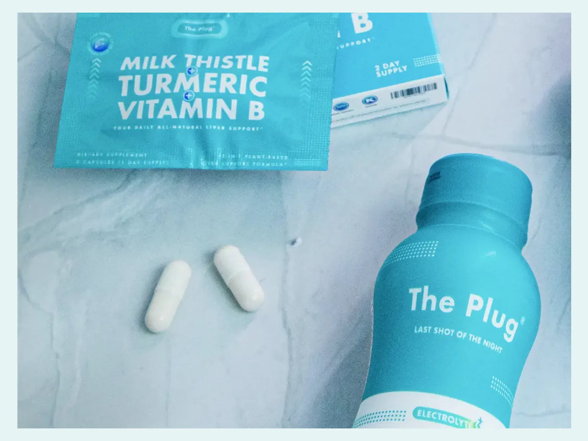 A bottle of The Plug Drink, two white capsules and a packet of The Plug Pills rest on a pale marble surface.