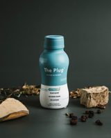 A bottle of The Plug Drink on a dark studio set