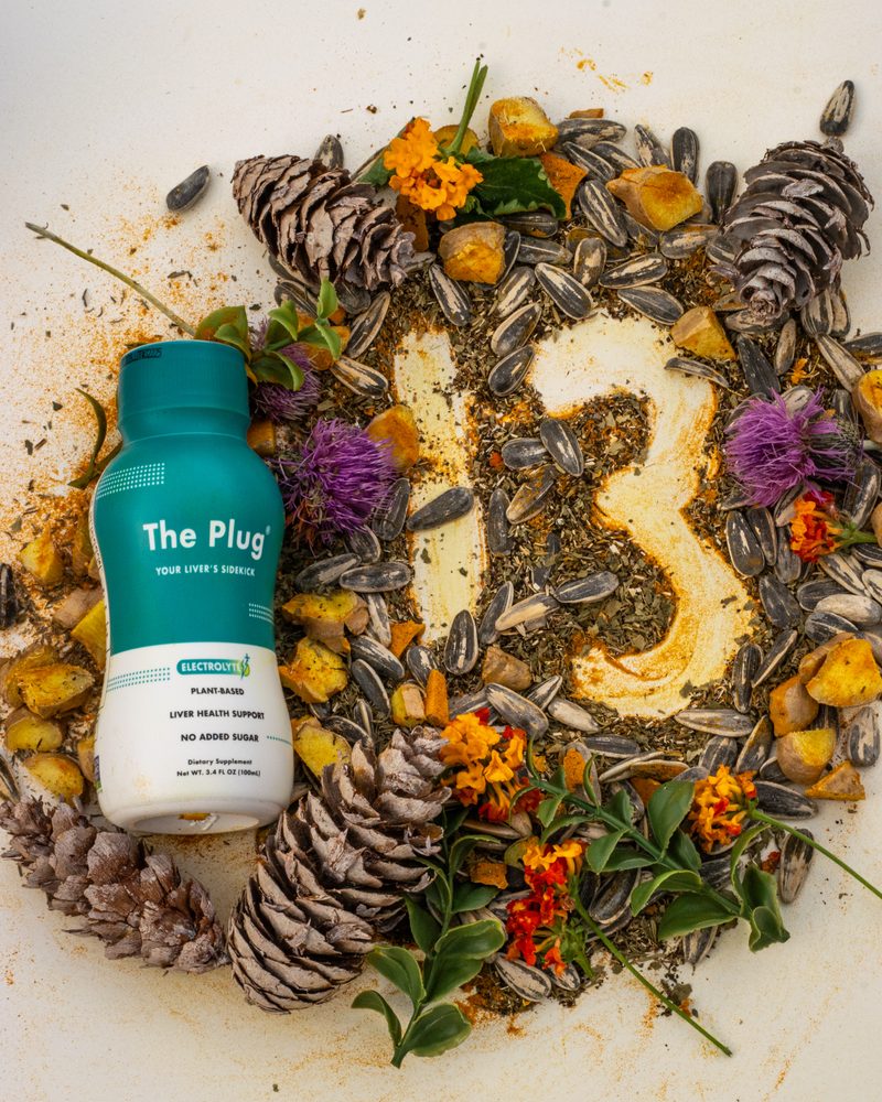 A bottle of The Plug Drink beside a 13 made of the blend's plants, flowers and seeds